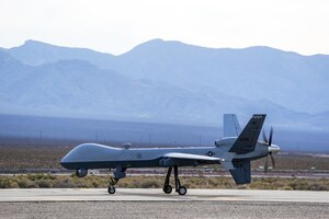 An aircraft moves along paved ground. Mountains are in the background.