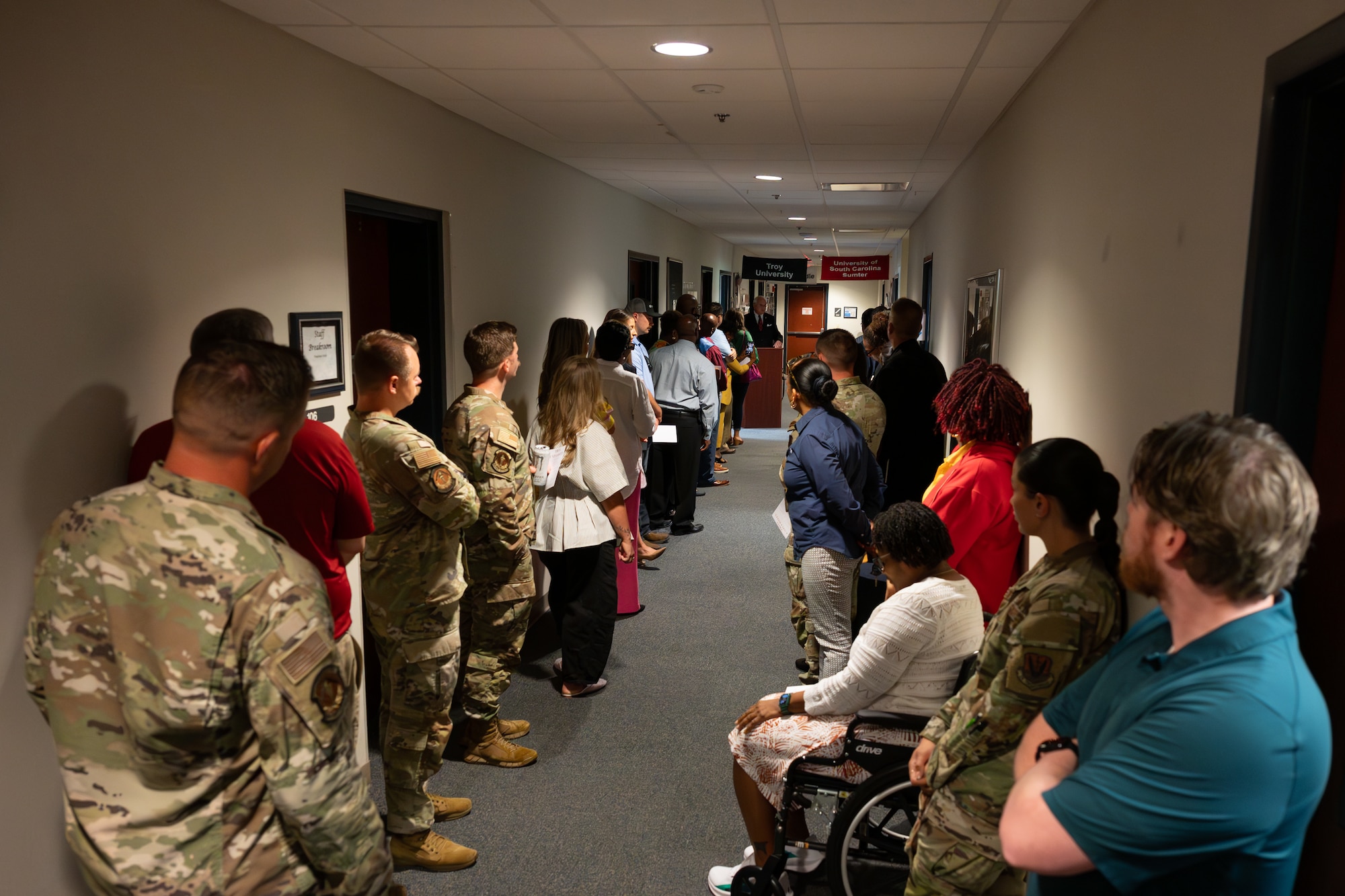U.S. Airmen, civilians and Troy University representatives gather in a hallway for the ribbon-cutting ceremony of Troy's new satellite office at Shaw Air Force Base, S.C., June 17, 2025.