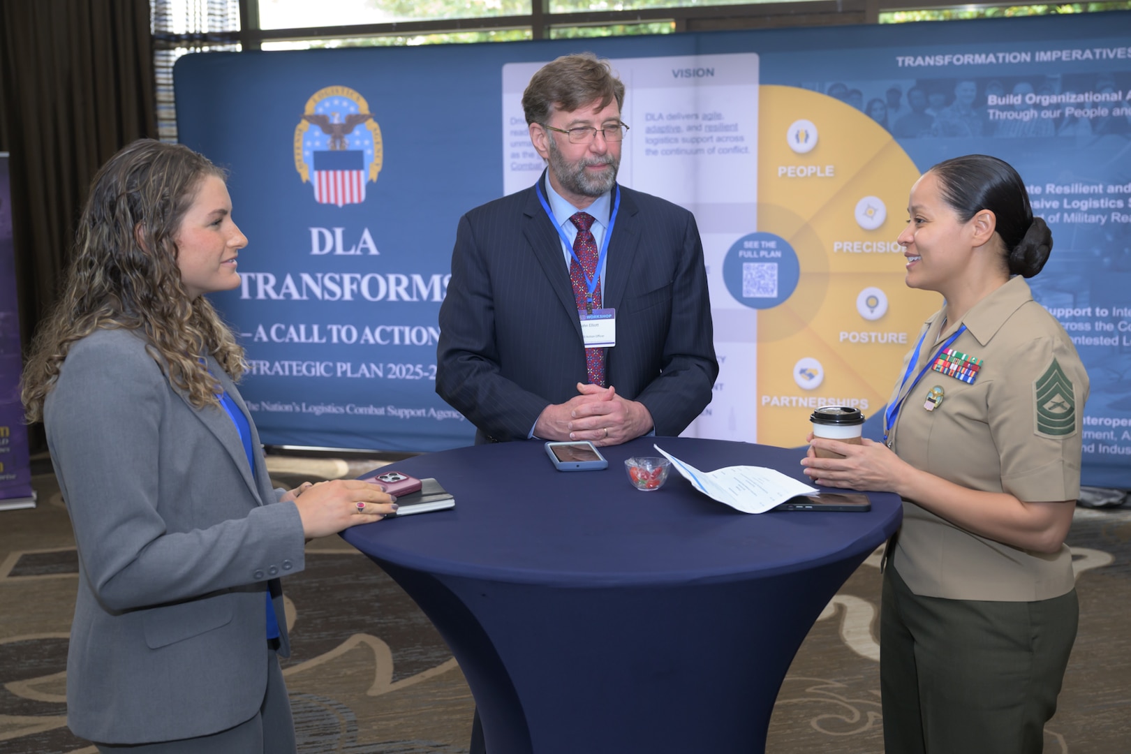 Man and 2 women standing at table in discussion.