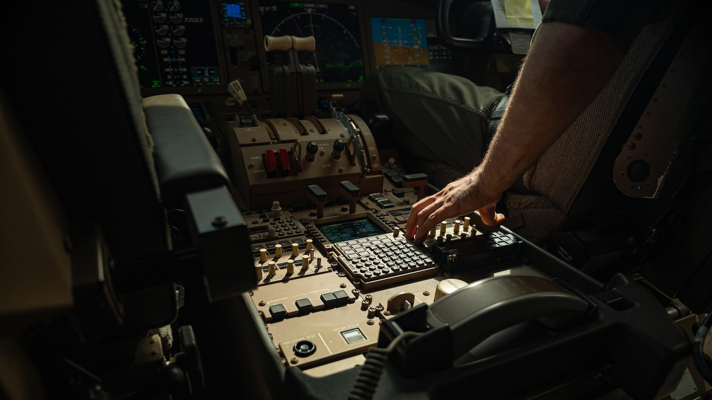 A pilot's hand reaches for controls in the flight deck of a KC-46