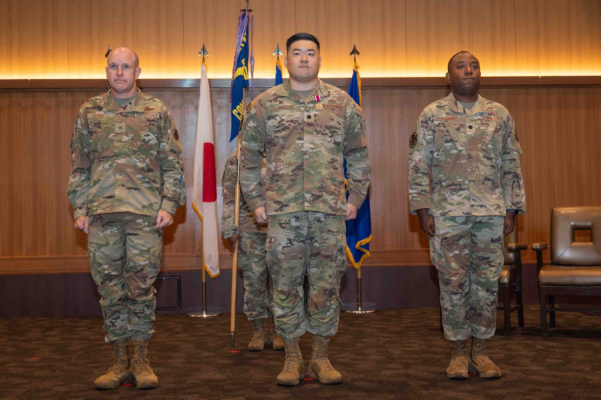 Three military member stand next to each other on a stage at a change of command ceremony