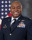 photo of uniformed US Airman standing in front of a US Flag.