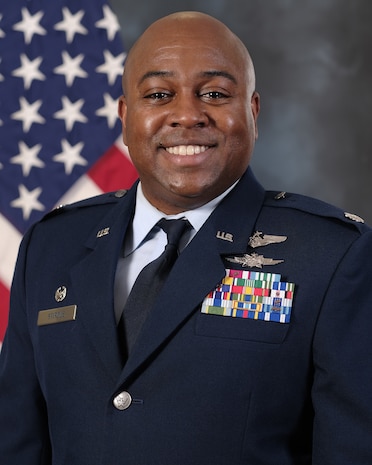 photo of uniformed US Airman standing in front of a US Flag.