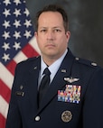 photo of uniformed US Airman standing in front of a US Flag.