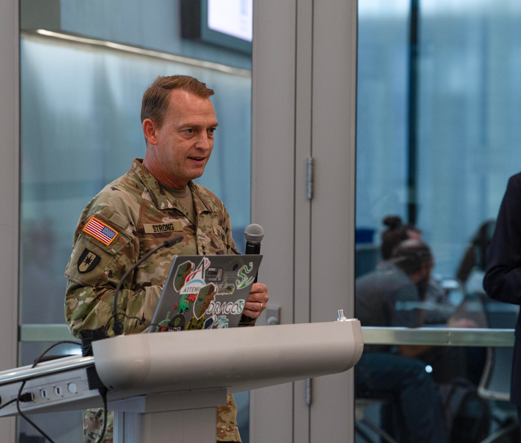 Army general in green uniform stands in front a podium hold mic and giving a speech.