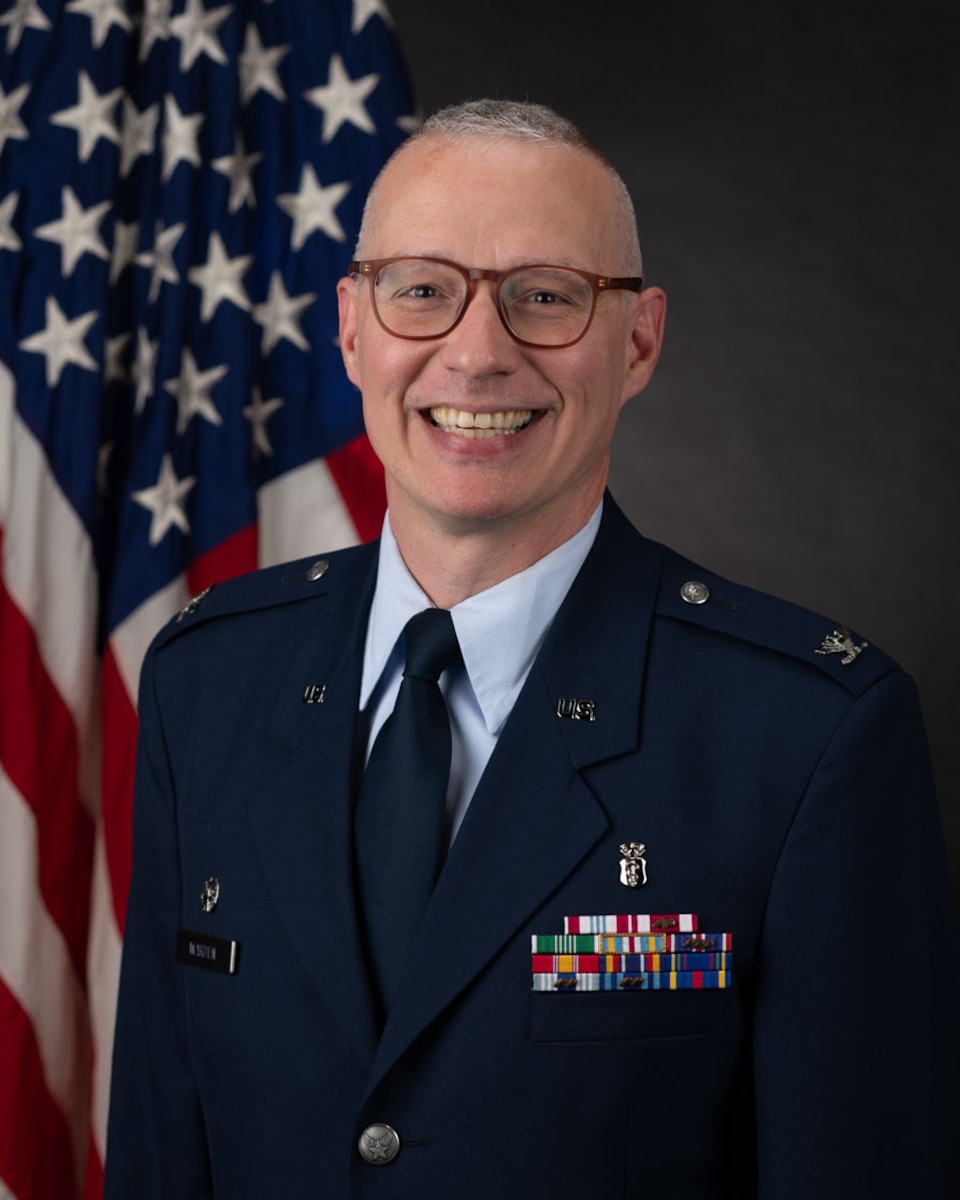 An individual in formal attire in front of the U.S. flag.