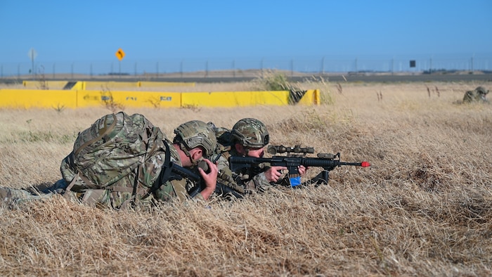 Tech. Sgt. Keiran Wilson (left) calls for pick-up at the Expeditionary Air Base (XAB) as a Defender from the 349th Security Forces Squadron (SFS) maintains security at the designated rendezvous point for extraction of the convoy during Exercise NEXUS RISING 25-01 at Travis AFB, Calif.