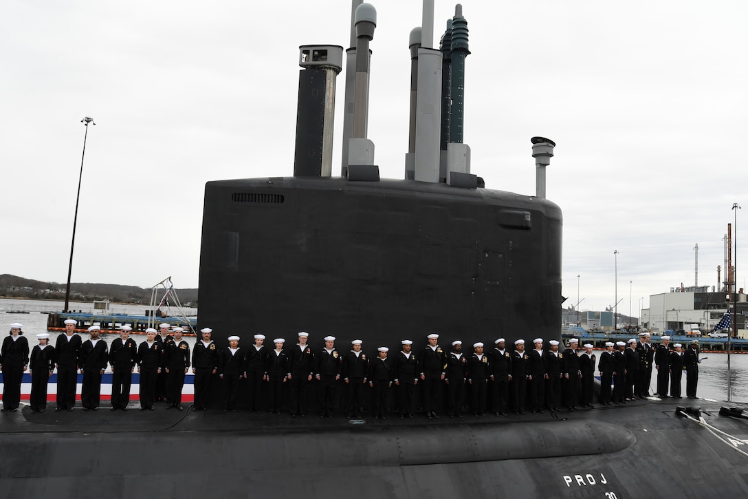 Sailors stand in a row atop a moored submarine.