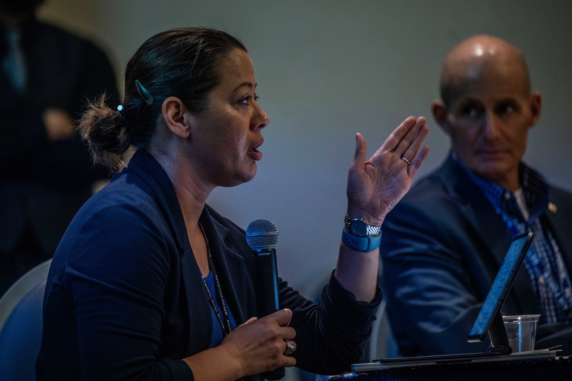 A woman with a microphone speaks to a room of people.