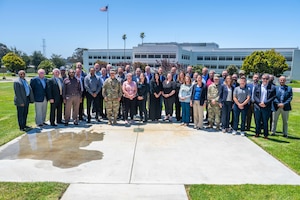 A group of people stand together for a photo outside on a sunny day.