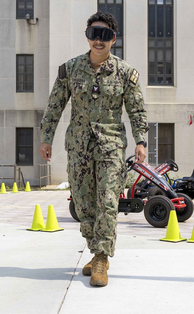 U.S. Navy Hospital Corpsman 3rd Class Jan Oseguera attempts to walk a straight line while wearing goggles simulating intoxication at the Annual Summer Safety Day event at Walter Reed National Military Medical Center on June 6, 2025. The event provides essential tips for staying safe and healthy during the summer months. (DOD photo by Roan Smith)