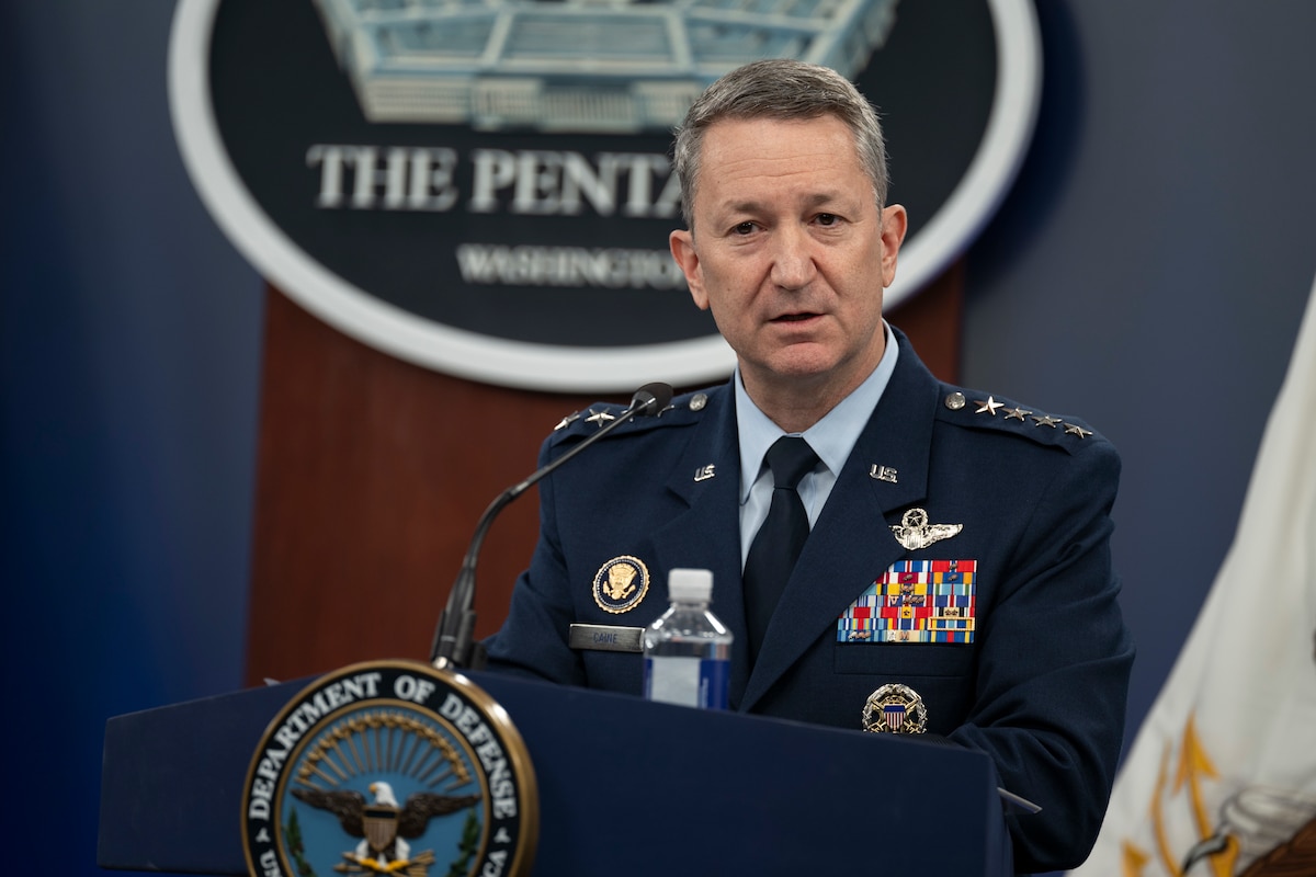 A man in a dress military uniform is speaking into a microphone from behind a podium.