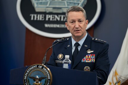 A man in a dress military uniform is speaking into a microphone from behind a podium.