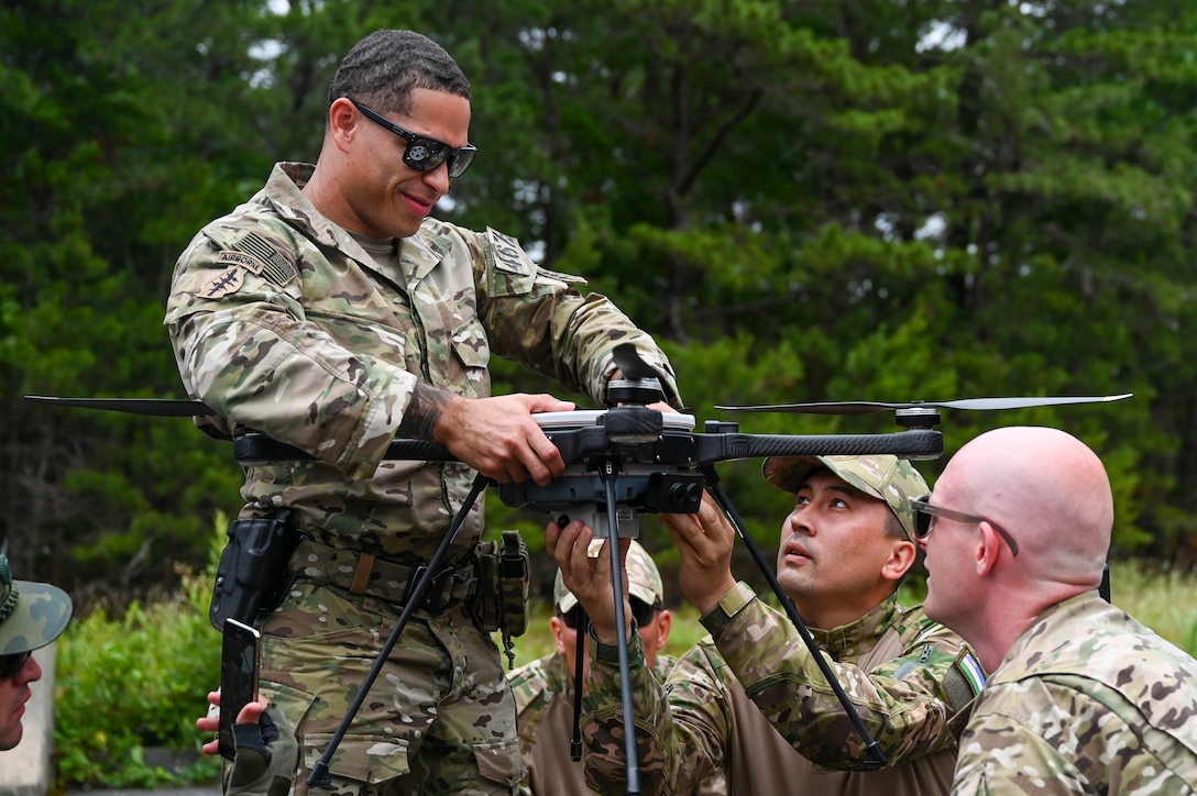 U.S. Army Sgt.1st Class Keshawn Burke, a team sergeant for the 646 Civil Affairs Team, stabilizes a recon drone so that an Uzbekistan soldier can secure a drone attachment at Joint Base Cape Cod, Massachusetts, June 19, 2025. During exercise Regional Cooperation 25. Regional Cooperation 25 is an annual, multinational U.S. Central Command sponsored command-post and field training exercise conducted by National Guard units in partnership with Central and South Asian nations. (U.S. Air Force photo by Staff Sgt. Colten Tessness)