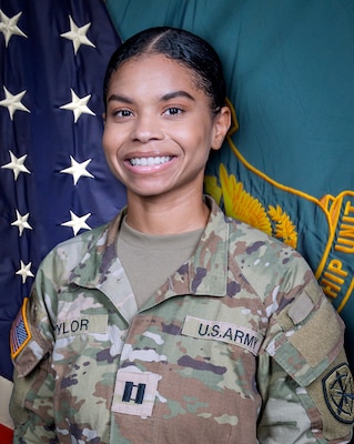 Woman in U.S. Army uniform standing in front of two flags.