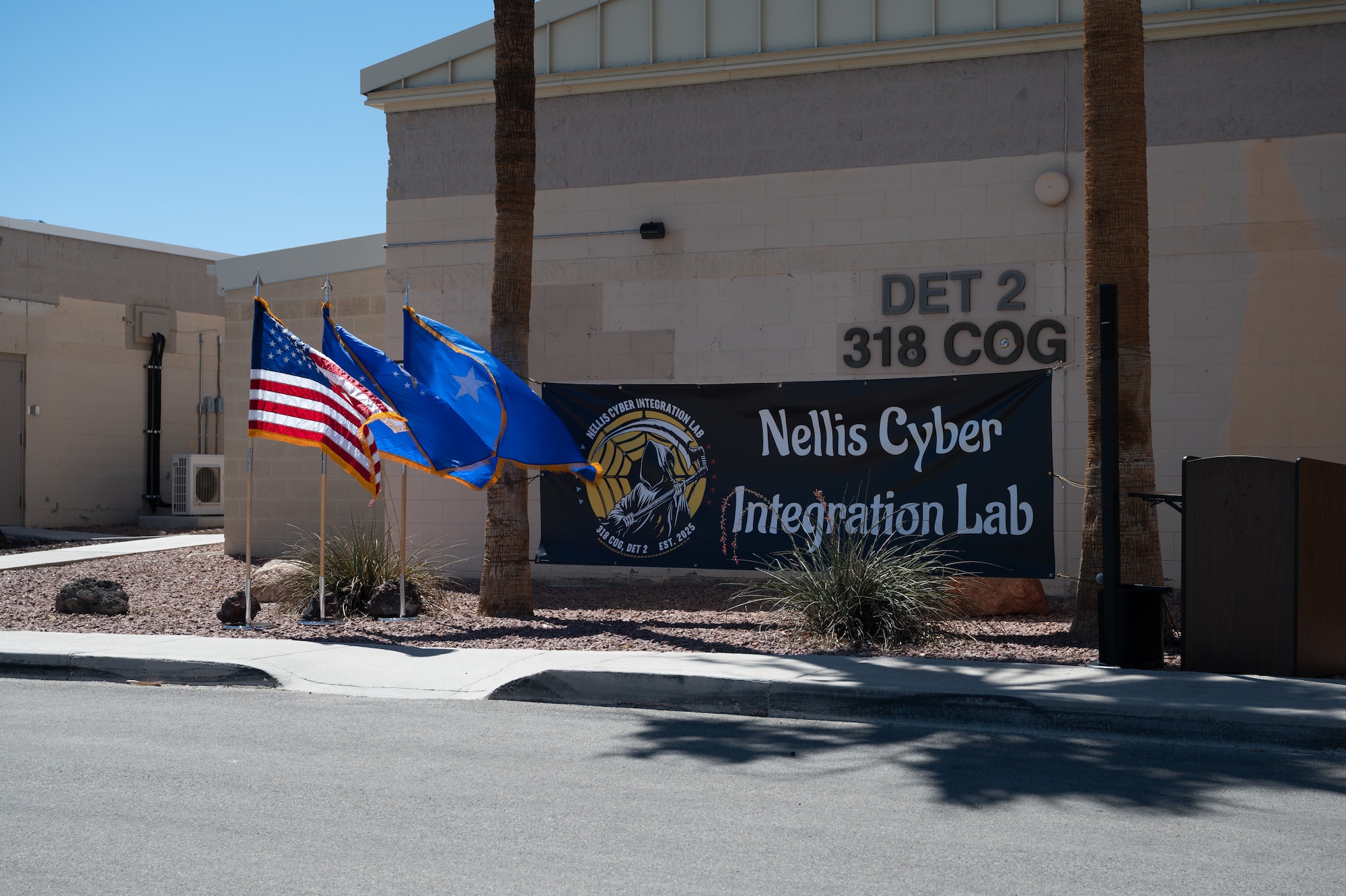 The outside of a military facility. Flags are blowing in the wind and there is a banner that reads 'Nellis Cyber Integration Lab.'