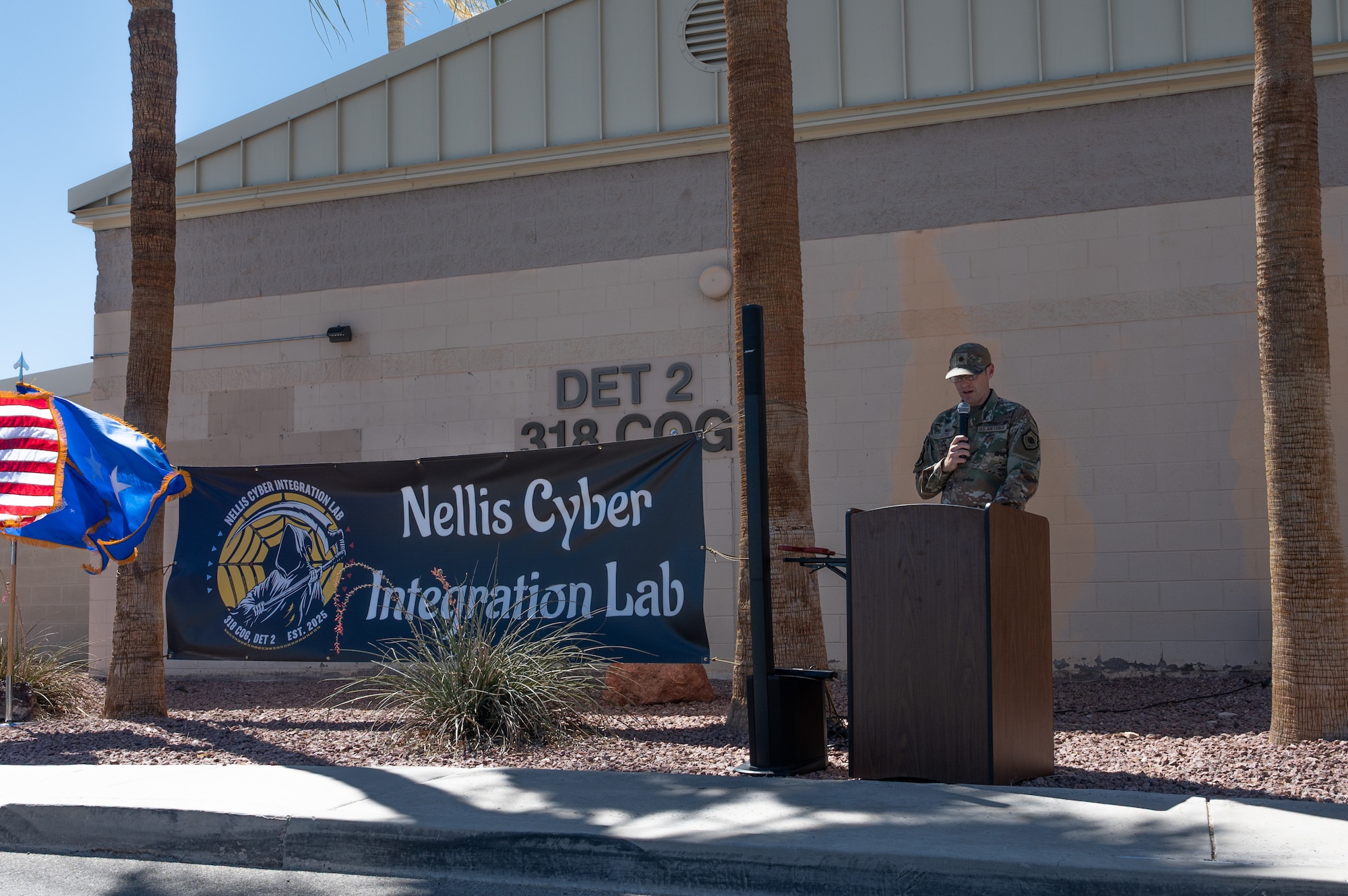 An Airman at a podium giving a speech in front of a military facility.