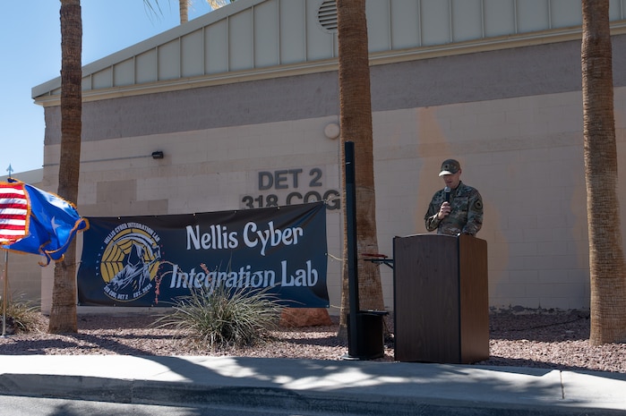 An Airman at a podium giving a speech in front of a military facility.