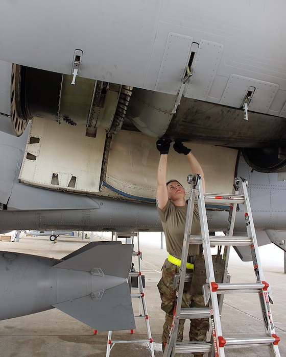 Female Airman with arms overhead, maintaining a jet engine.