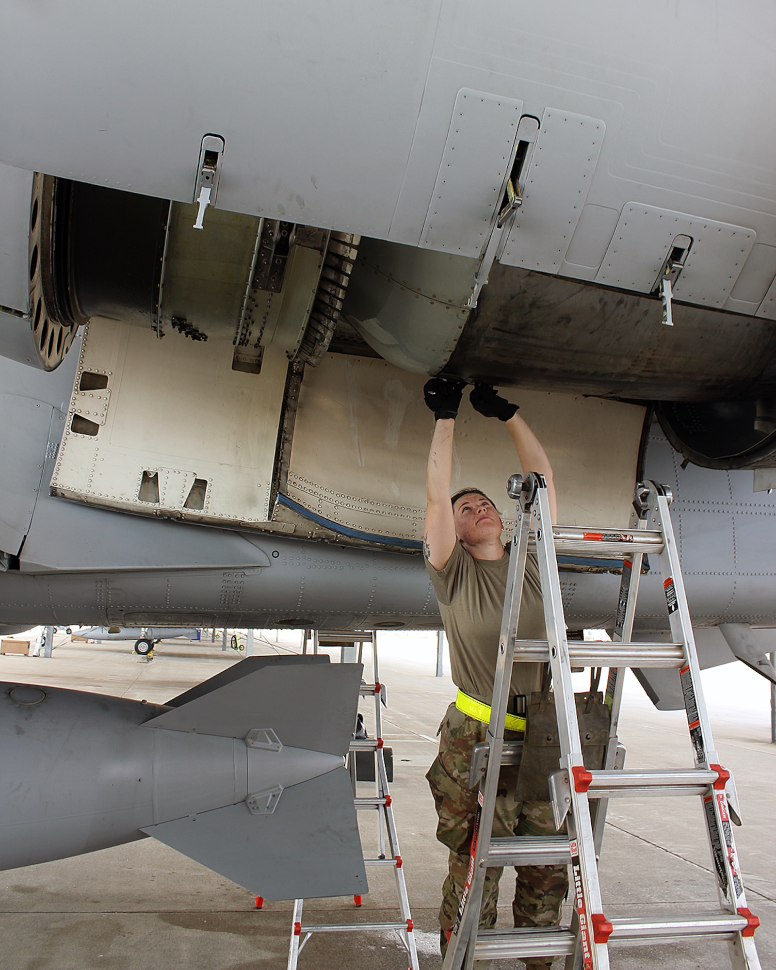 Female Airman with arms overhead, maintaining a jet engine.