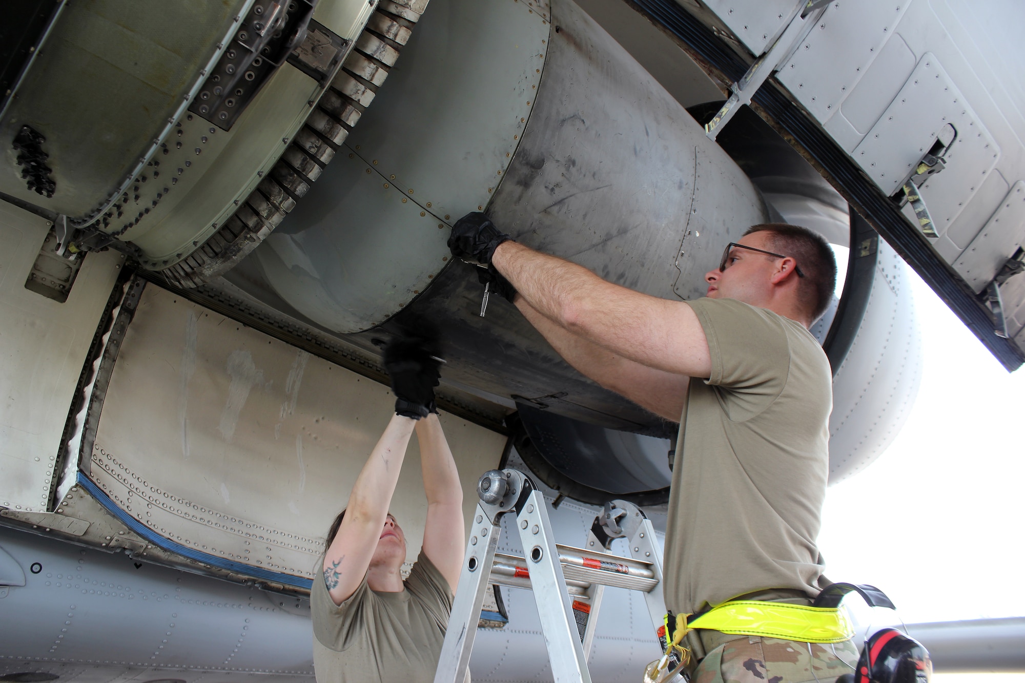 Two Airmen with hands above them in jet engine.