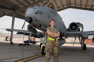 Female Airman standing in front of A-10 with arms crossed, smiling.