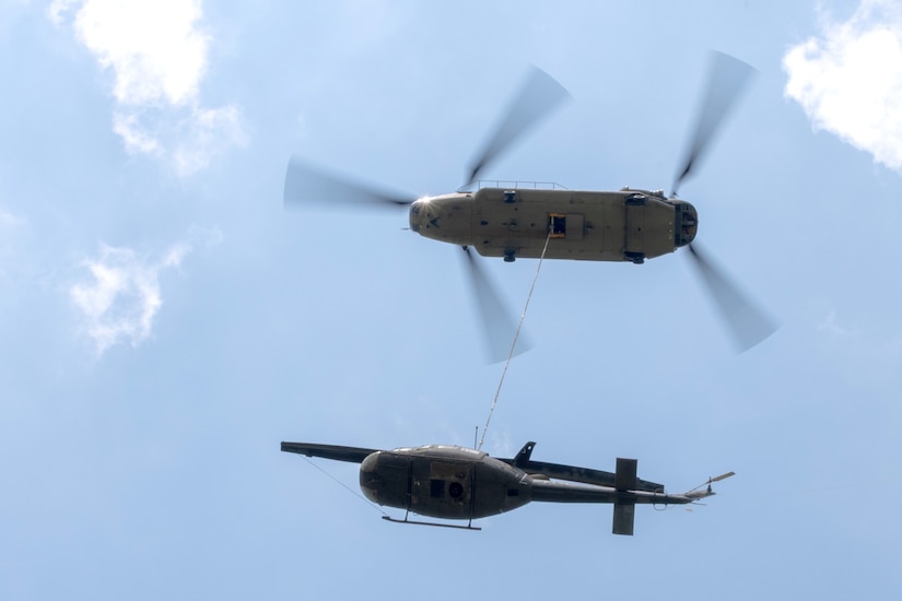 A CH-47 Chinook helicopter from 2-104th General Support Aviation Battalion, 28th Expeditionary Combat Aviation Brigade airlifts a decommissioned UH-1 “Huey” helicopter from the top Blue Mountain near Fort Indiantown Gap, Pennsylvania, to the installation on June 20, 2025. (Pennsylvania National Guard photo by Wayne V. Hall)