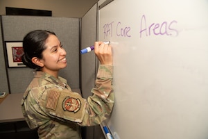 A military member smiles and writes down information on a dry erase board