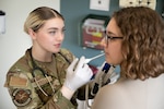 Uniformed service member holds thermometer in a patient's mouth.
