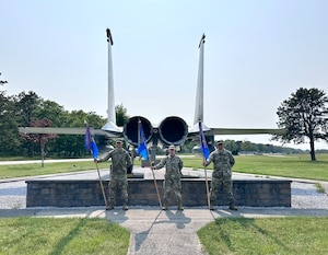 A group of Airmen, in a formation outside, pay respects to the American flag.