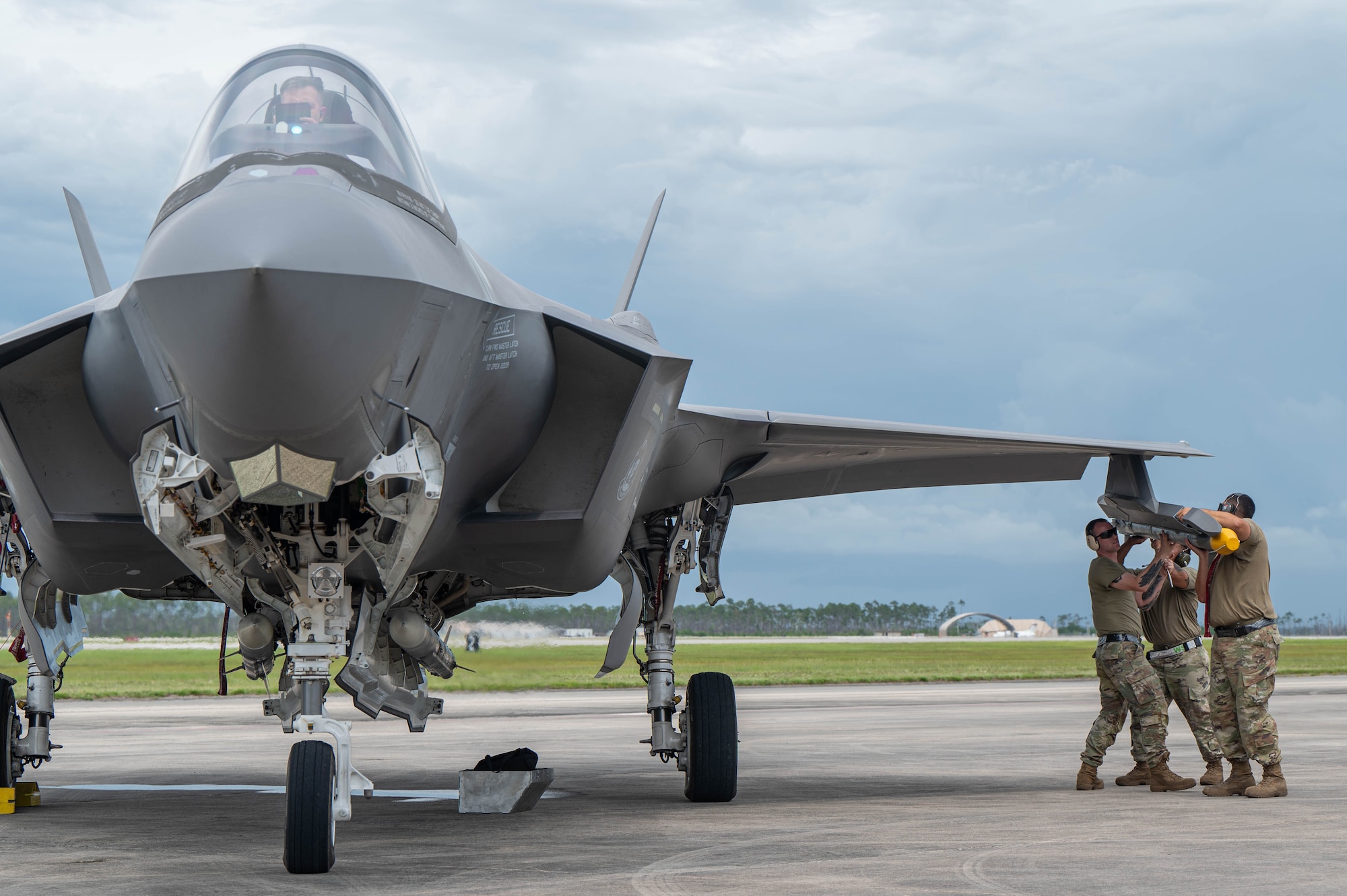 Three Airmen load munitions onto and F-35 during a hot ICT
