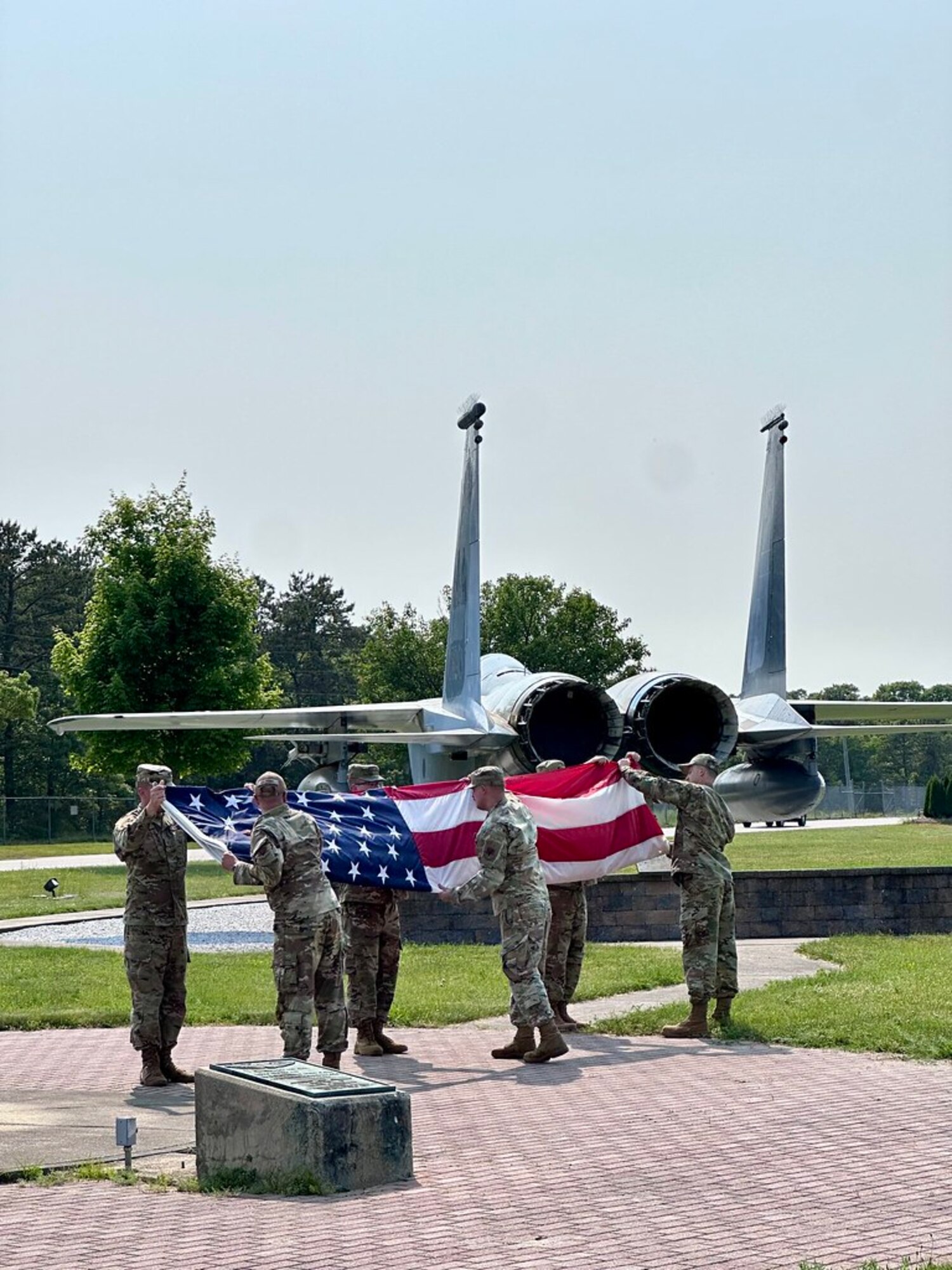 A group of Airmen, in a formation outside, pay respects to the American flag.