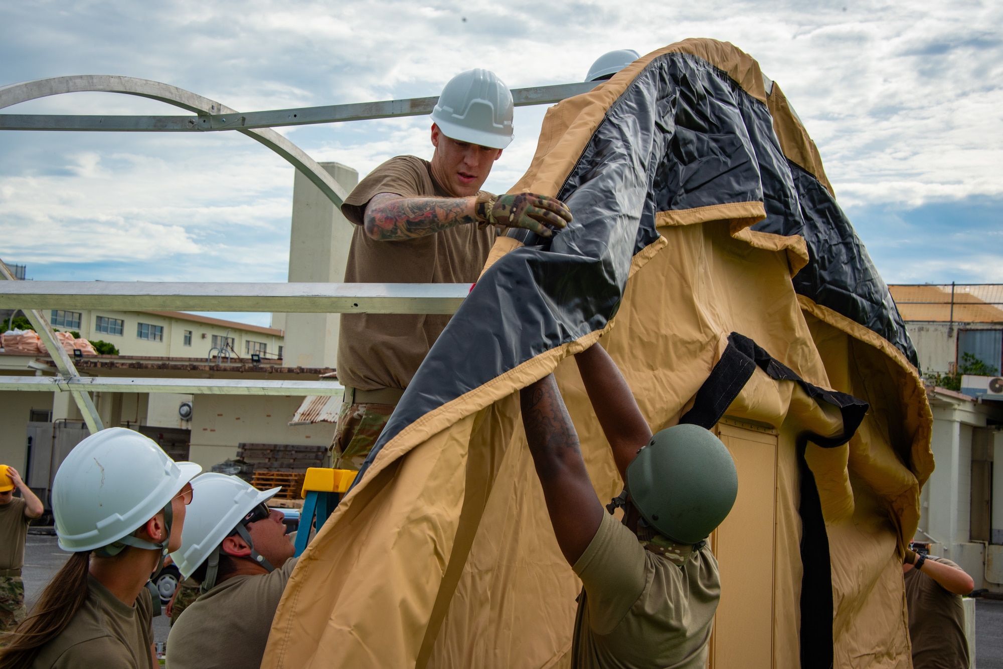 U.S. Air National Guardsmen assigned to the 134th Force Support Squadron and U.S. Air Force Airmen assigned to the 718th FSS position the outer shell of a tent during a joint training event at Kadena Air Base, Japan, June 18, 2025. Working side by side, Airmen from both components sharpen their ability to rapidly establish shelters in austere environments. (U.S. Air National Guard photo by Staff Sgt. Jesse Hanson)