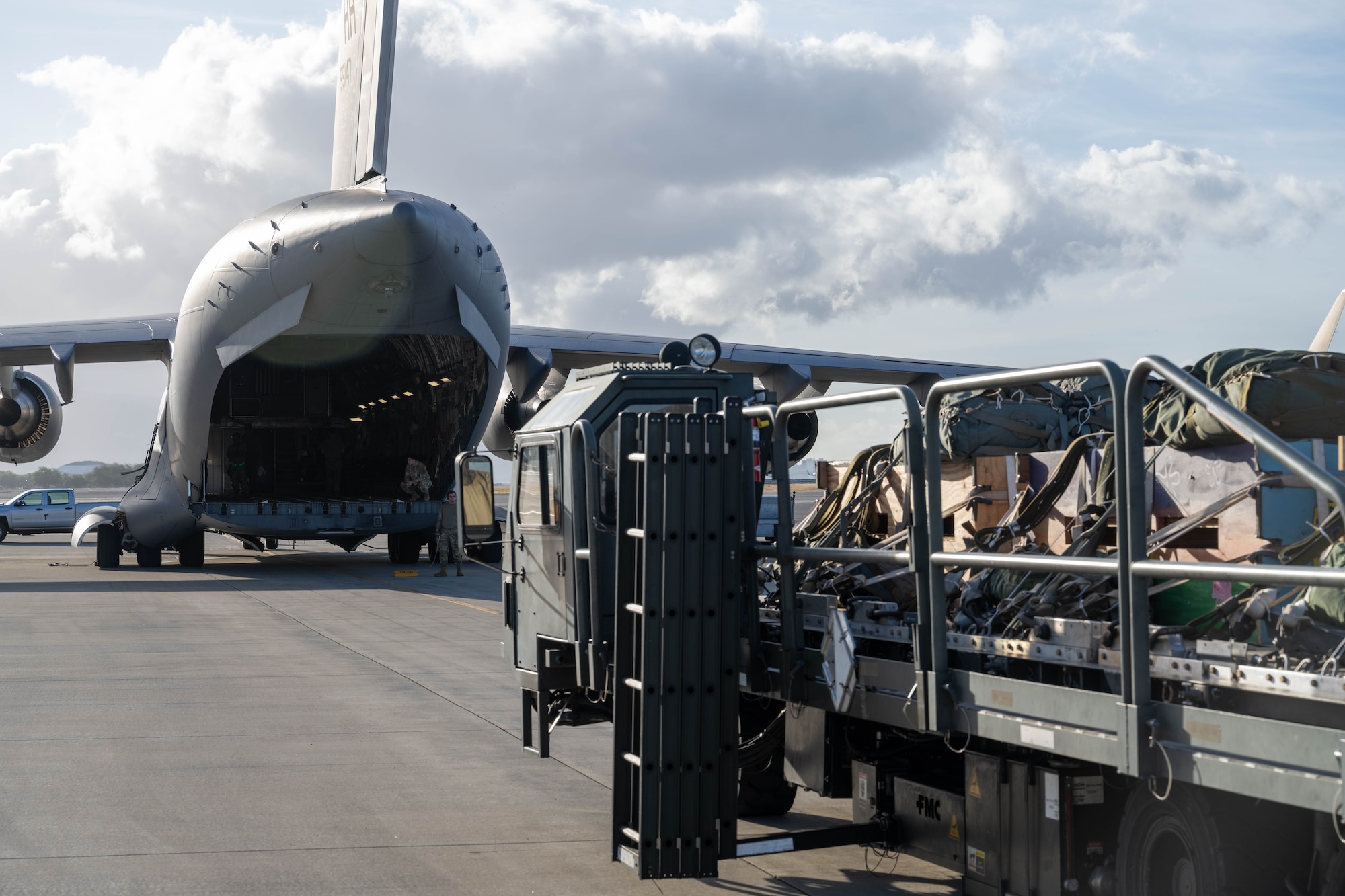 A K-loader position itself behind a C-17 Globemaster III to load cargo for an airdrop.