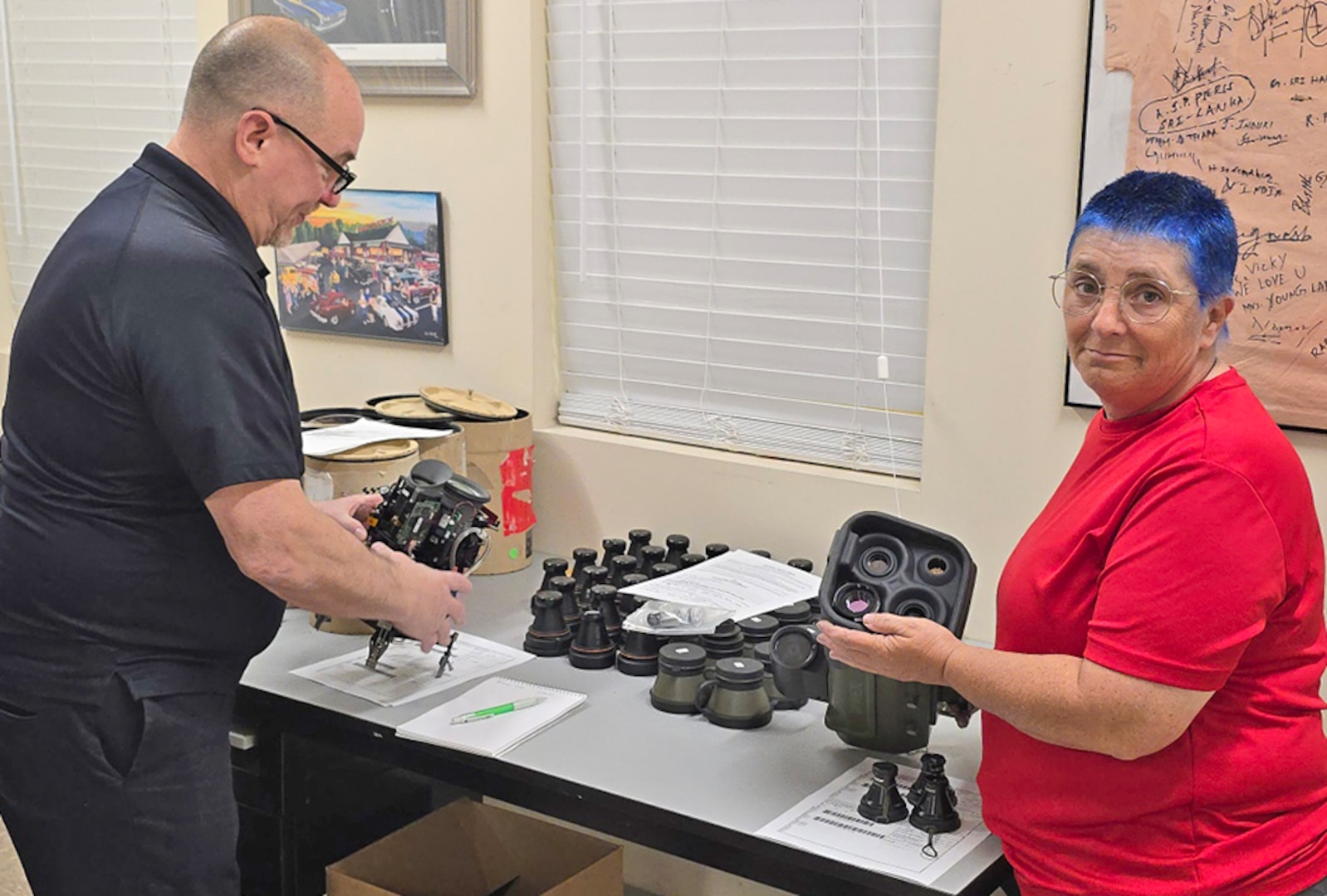 A man and a woman evaluate used military optics in an office space.