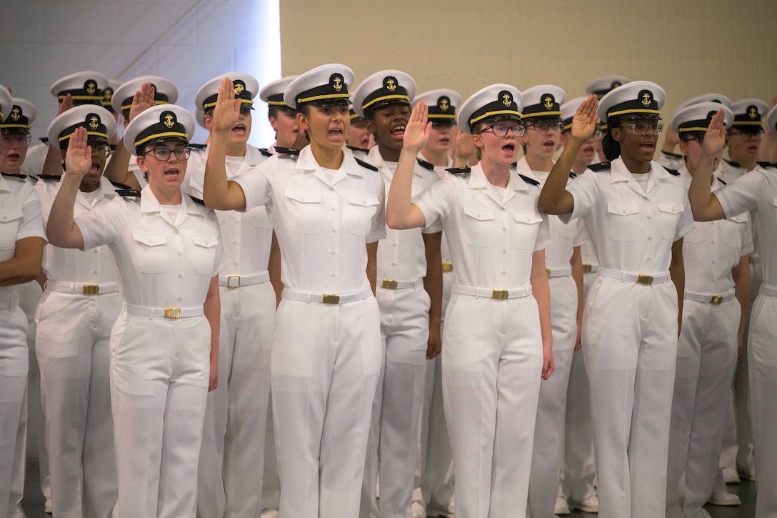 A group of midshipman candidates stand in a group and raise their right hands.