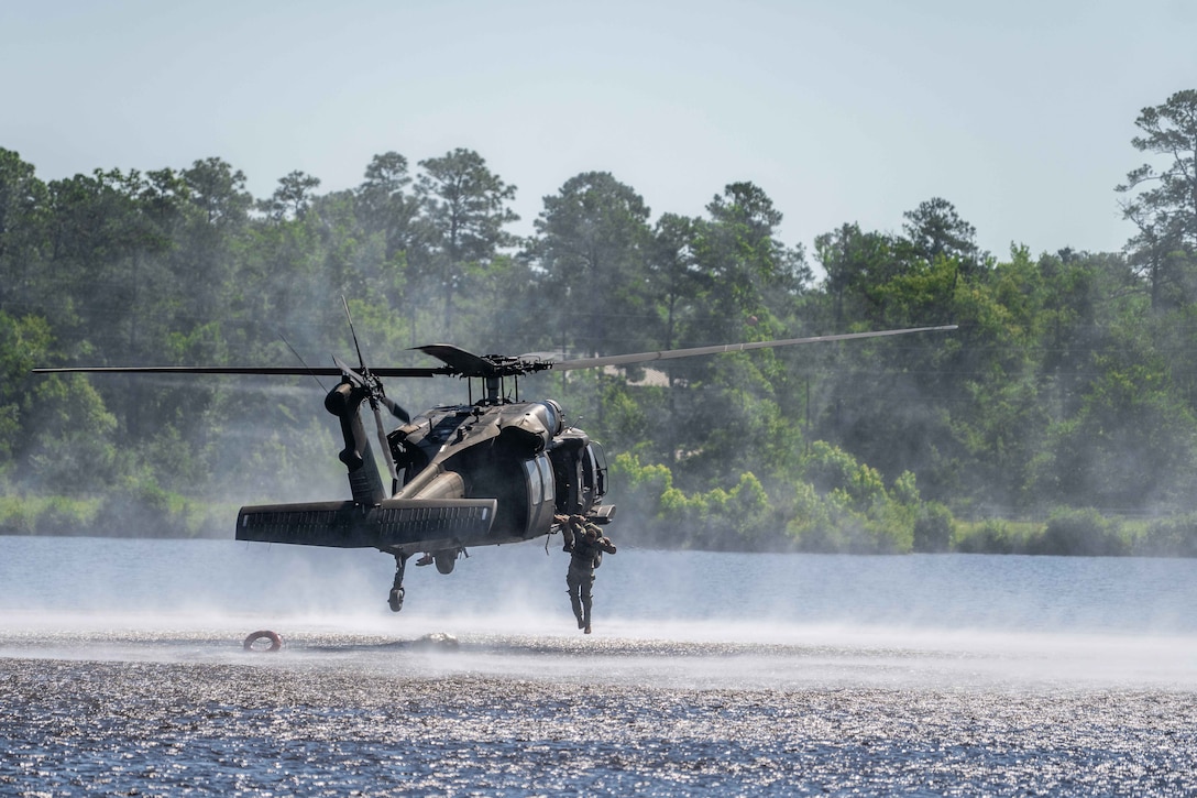 A soldier jumps from a helicopter into a pond on a sunny day.