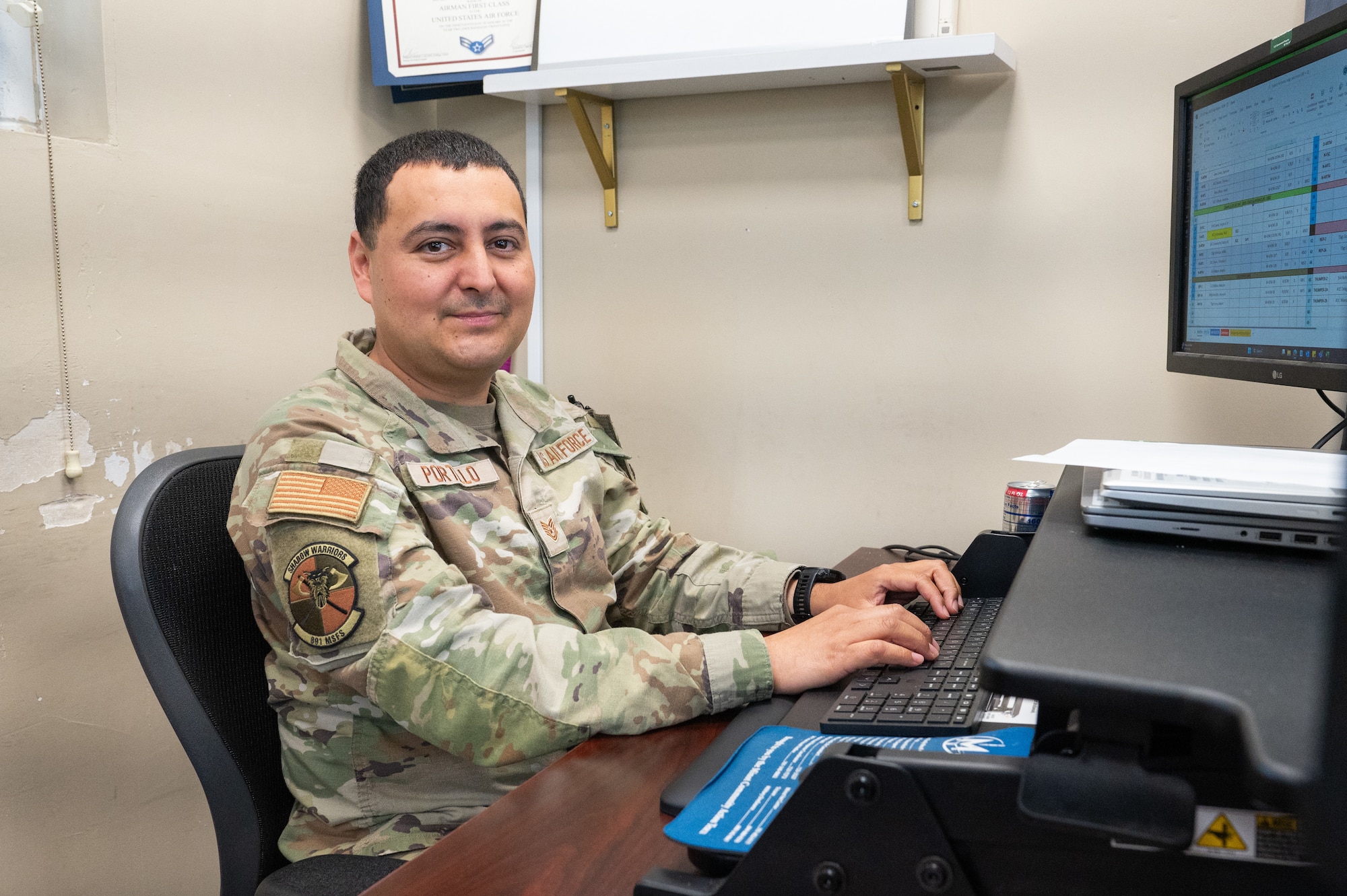 An Airman poses for a photo in front of a computer.