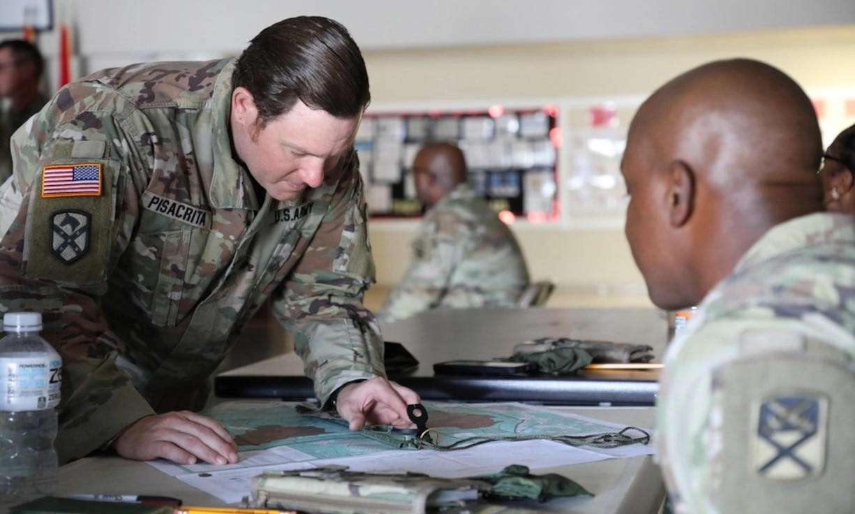 Male US Soldier points to a map while another male US Soldier looks on during a map training exercise