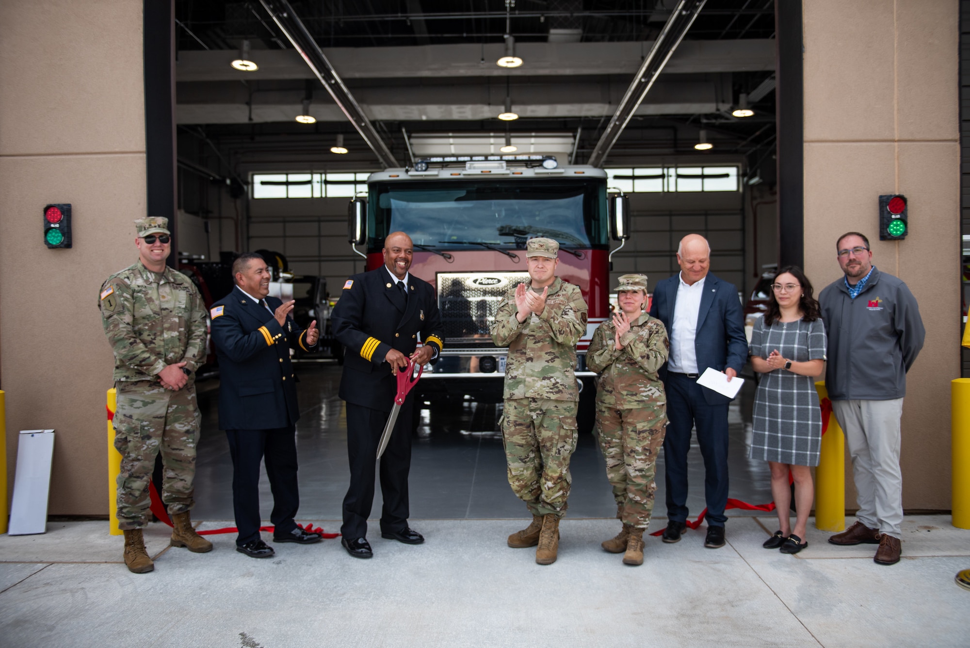 group of civilian and military members applaud after cutting ribbon in front of fire truck