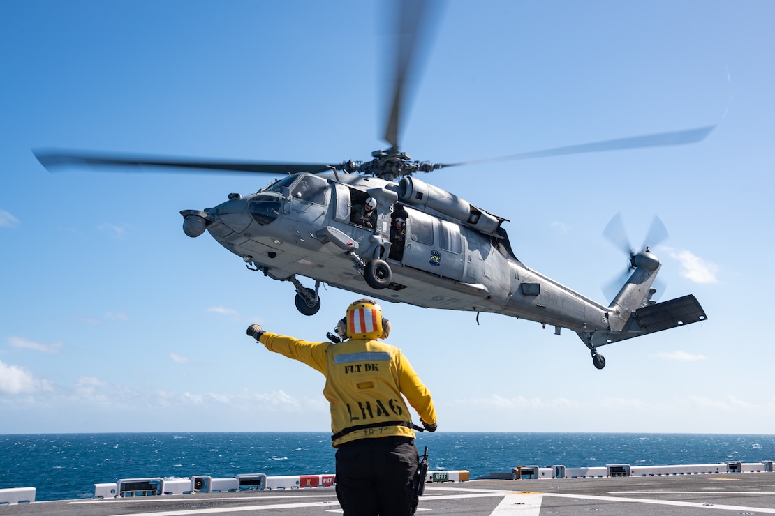 Aviation Boatswain’s Mate (Handling) 1st Class Rebekah Hood, from Gilbert, Arizona, assigned to the forward-deployed amphibious assault ship USS America (LHA 6) directs an MH-60S Seahawk from Helicopter Sea Combat Squadron (HSC) 25 on the flight deck of the America while conducting flight operations in the Tasman Sea, June 20.
