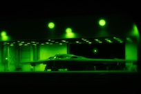 A view through night vision of a flat, triangular-looking military aircraft sitting in a hangar.