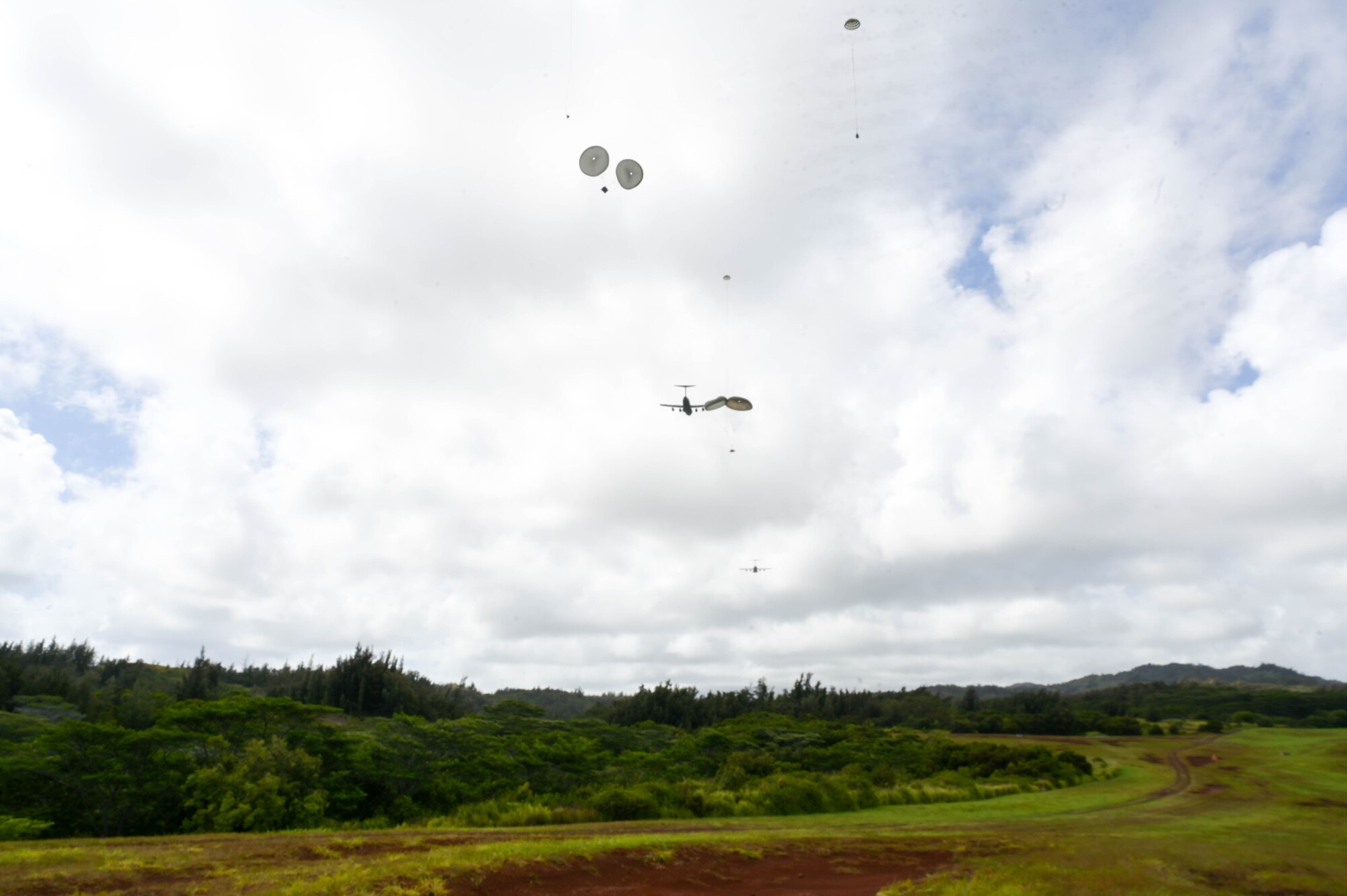 Two U.S. Air Force C-17 Globemaster IIIs drop cargo over a drop zone on Oahu, Hawaii.