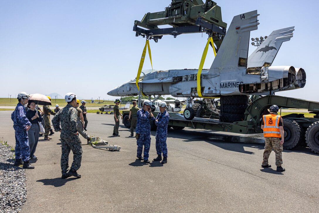 U.S. Marines with Aircraft Rescue and Firefighting, Headquarters and Headquarters Squadron, Marine Corps Air Station Iwakuni, Japan Air Self-Defense Force members with 5th and 6th Air Wing, Japan Maritime Self-Defense Force members with Fleet Air Wing 31, Royal Airmen with Joint Aircraft Recovery Transportation Squadron, observe an F/A-18C Hornet being lowered onto a truck during Crash Damaged or Disabled Aircraft Recovery training at Marine Corps Air Station Iwakuni, Japan, June 5, 2025. CDDAR training was held for the first time at MCAS Iwakuni by the F-35 Joint Program Office to bring multiple nations together to enhance aircraft recovery and rescue techniques and capabilities across North Atlantic Treaty Organization Allies. (U.S. Marine Corps photo by Cpl. Dahkareo Pritchett)