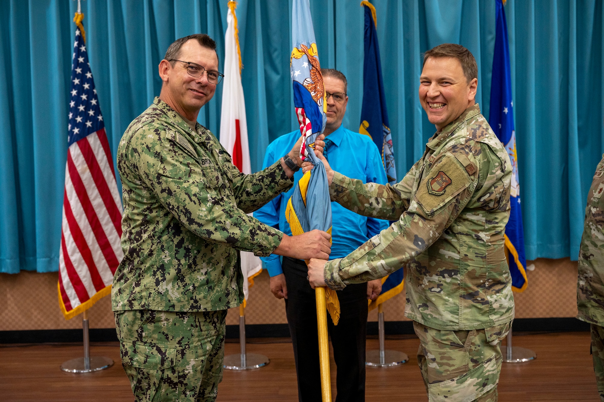 U.S. Navy Capt. Patrick Brown, Defense Logistics Agency Indo-Pacific commander, left, passes the guidon to U.S. Air Force Maj. Dominic Baker, DLA Energy Okinawa incoming commander, right, during a change of command ceremony at Kadena Air Base, Japan, June 18, 2025.