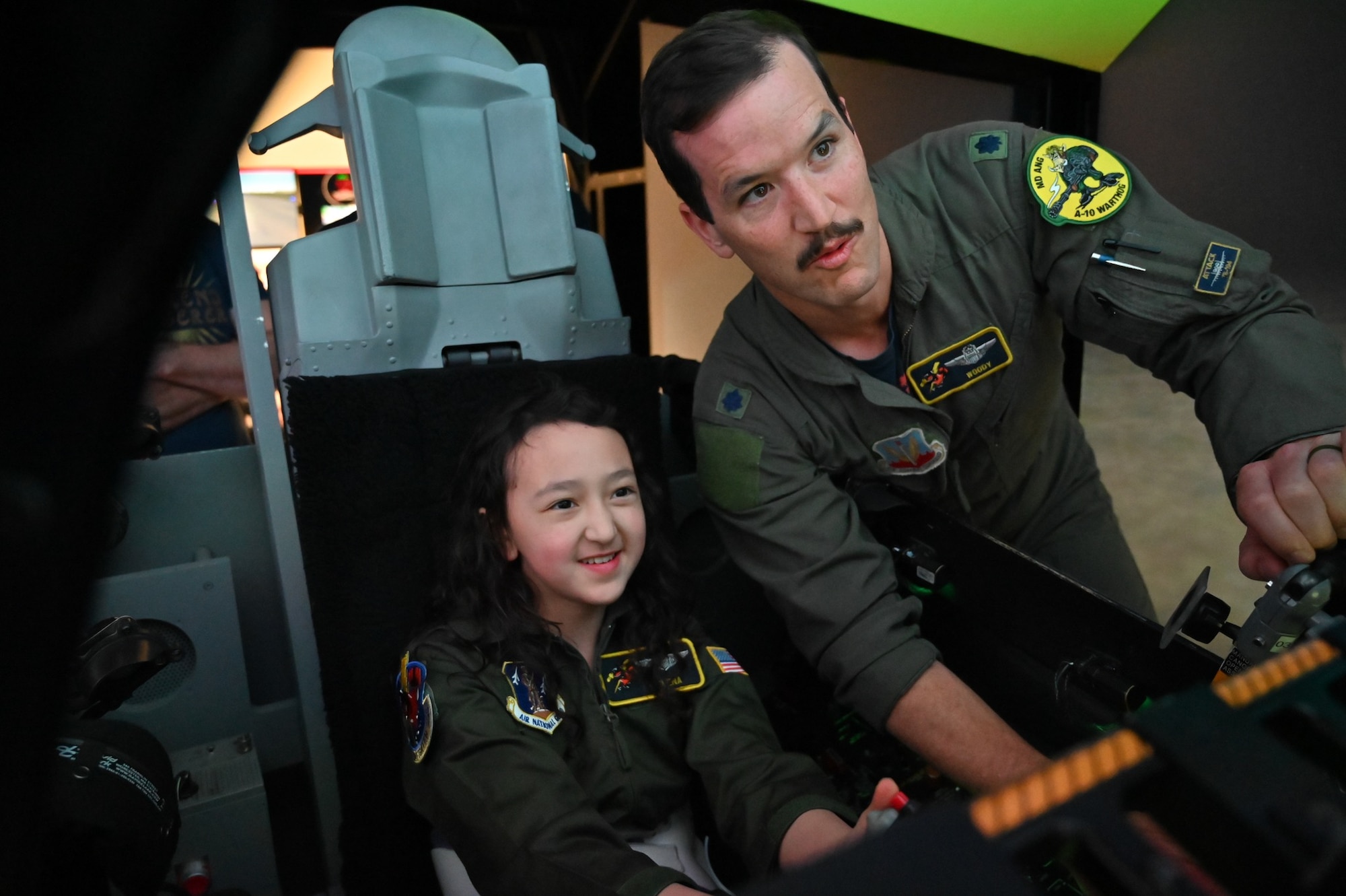Maryland Air National Guard Lt. Col. Daniel Griffin, an A-10C Thunderbolt II pilot assigned to the 104th Fighter Squadron, teaches Elena LeMoine how to use an A-10 flight simulator at Warfield Air National Guard Base at Martin State Airport, Maryland, June 7, 2025. LeMoine and her family attended "Pilot For a Day," facilitated by the Gold in Fight Foundation, which invites children and families from the local community who have catastrophic illnesses to spend the day with pilots. (U.S. Air National Guard Photo by Staff Sgt. Laura Virtue)