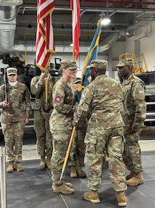 The commander of the 405th Army Field Support Brigade, Col. Ernest Lane II, passes the AFSBn-Poland colors to the incoming commander, Lt. Col. Michelle McDevitt, during the AFSBn-Poland change of command ceremony June 25, 2025, at the Powidz Army Prepositioned Stocks-2 worksite.