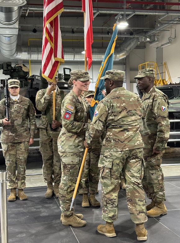 The commander of the 405th Army Field Support Brigade, Col. Ernest Lane II, passes the AFSBn-Poland colors to the incoming commander, Lt. Col. Michelle McDevitt, during the AFSBn-Poland change of command ceremony June 25, 2025, at the Powidz Army Prepositioned Stocks-2 worksite.