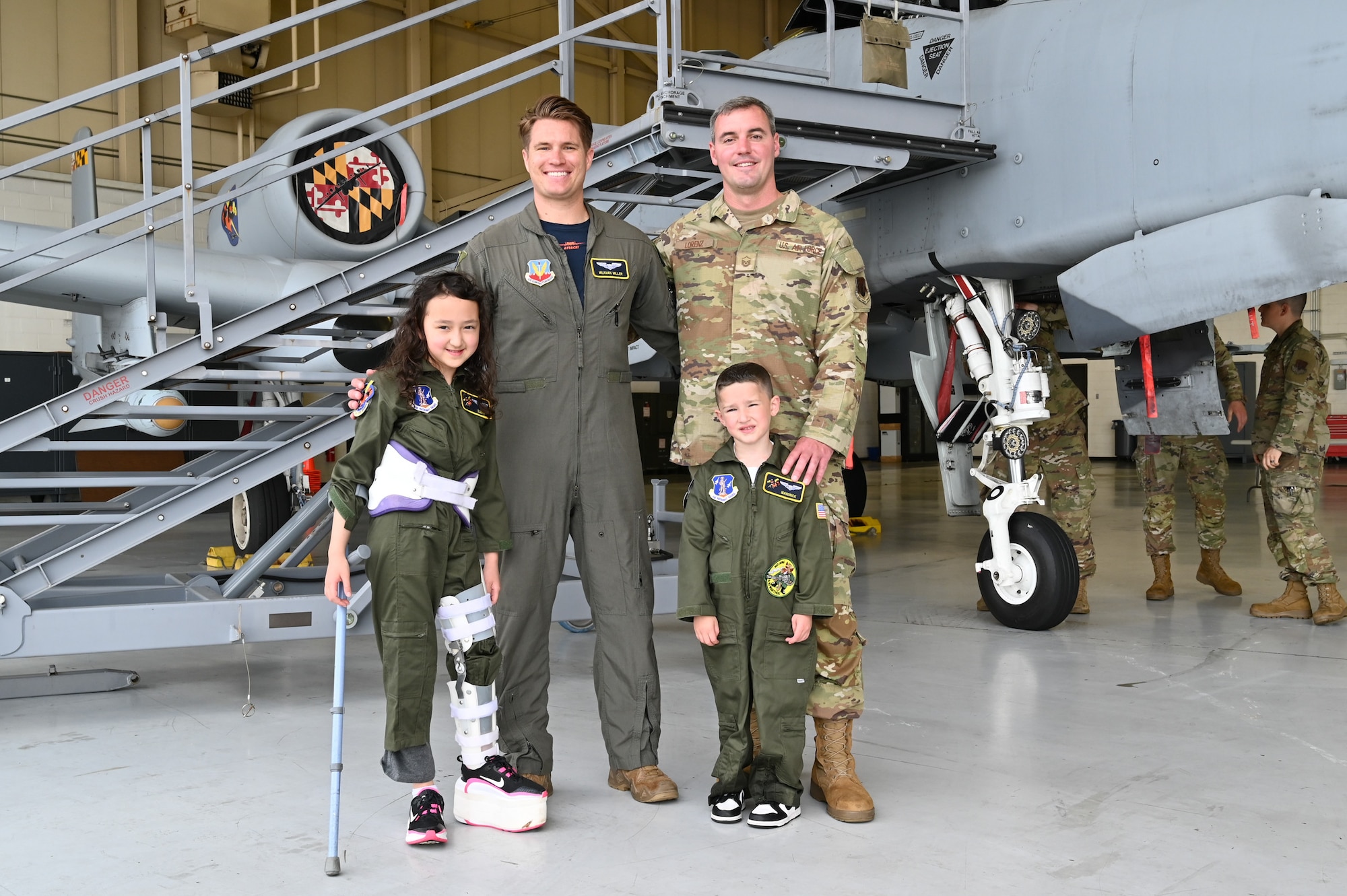 Maryland Air National Guard Capt. Carson Miller (middle-left), an A-10C Thunderbolt ll pilot assigned to the 104th Fighter Squadron, Master Sgt. Jonathan Lorenz (middle-right), avionics technician for the 175th Maintenance Squadron, and Elena LeMoine (left) and Maverick Bell (right), pose for a group photo in front of an A-10C Thunderbolt II static display at Warfield Air National Guard Base at Martin State Airport, Maryland, June 7, 2025. LeMoine and Bell, as well as their families, attended "Pilot For a Day," facilitated by the Gold in Fight Foundation, which invites children and families from the local community who have catastrophic illnesses to spend the day with pilots. (U.S. Air National Guard Photo by Staff Sgt. Laura Virtue)