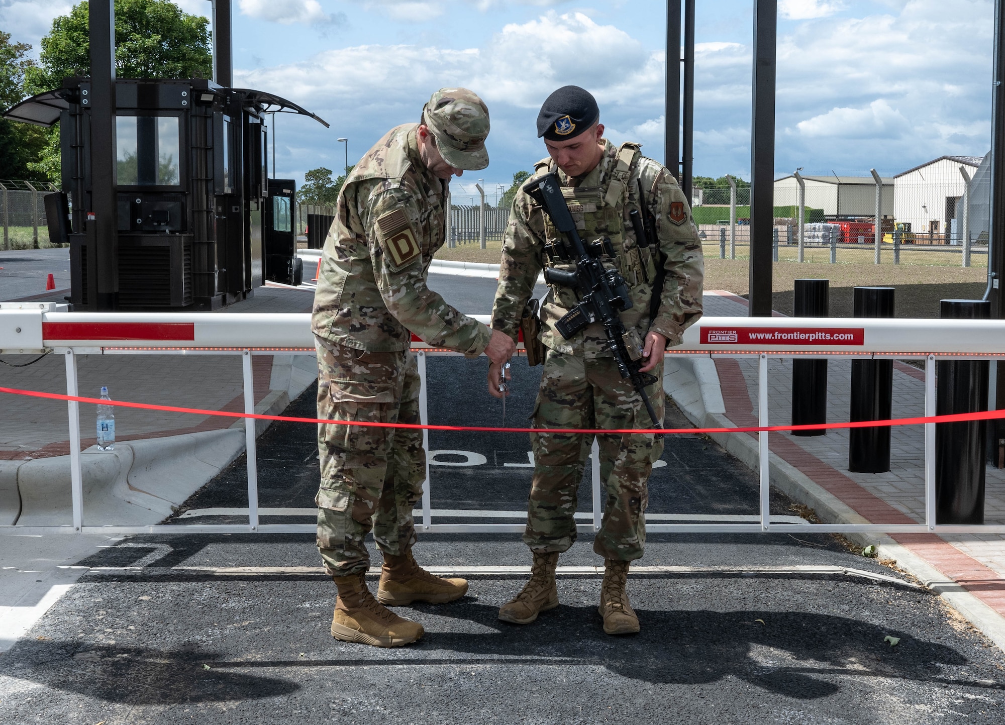 U.S. Air Force Col. Ryan Garlow, left, 100th Air Refueling Wing commander, and Airman Jonah Kniss, 100th Security Forces Squadron response force member, cut the ribbon during the new gate reveal at RAF Mildenhall, England, June 24, 2025.
